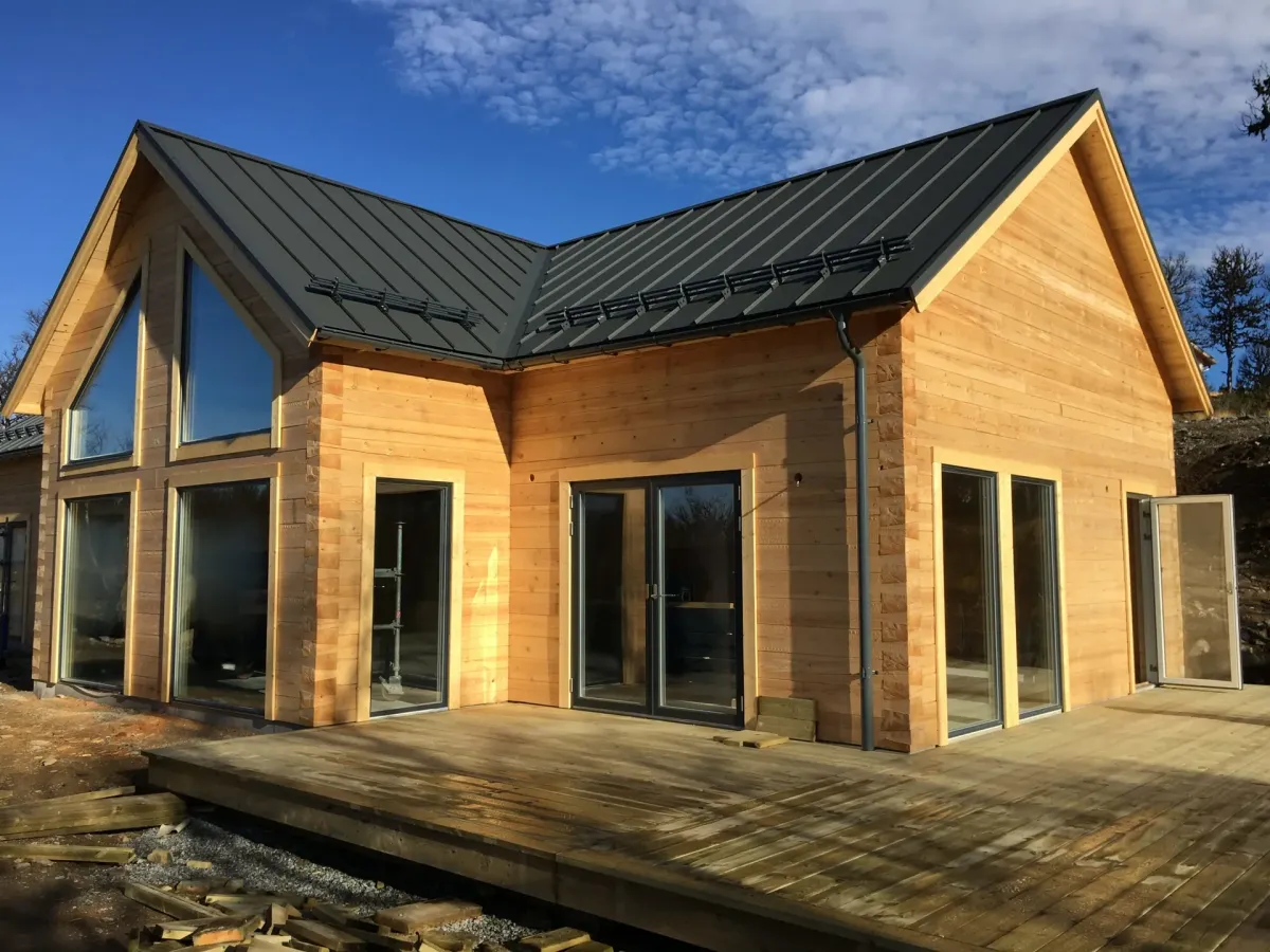 Nybyggt trähus med svart plåttak och stora fönster, byggt i Dalarna och Härjedalen.